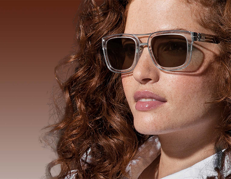 Eine junge Frau mit roten, lockigen Haaren trägt eine Sonnenbrille mit transparenter Fassung
